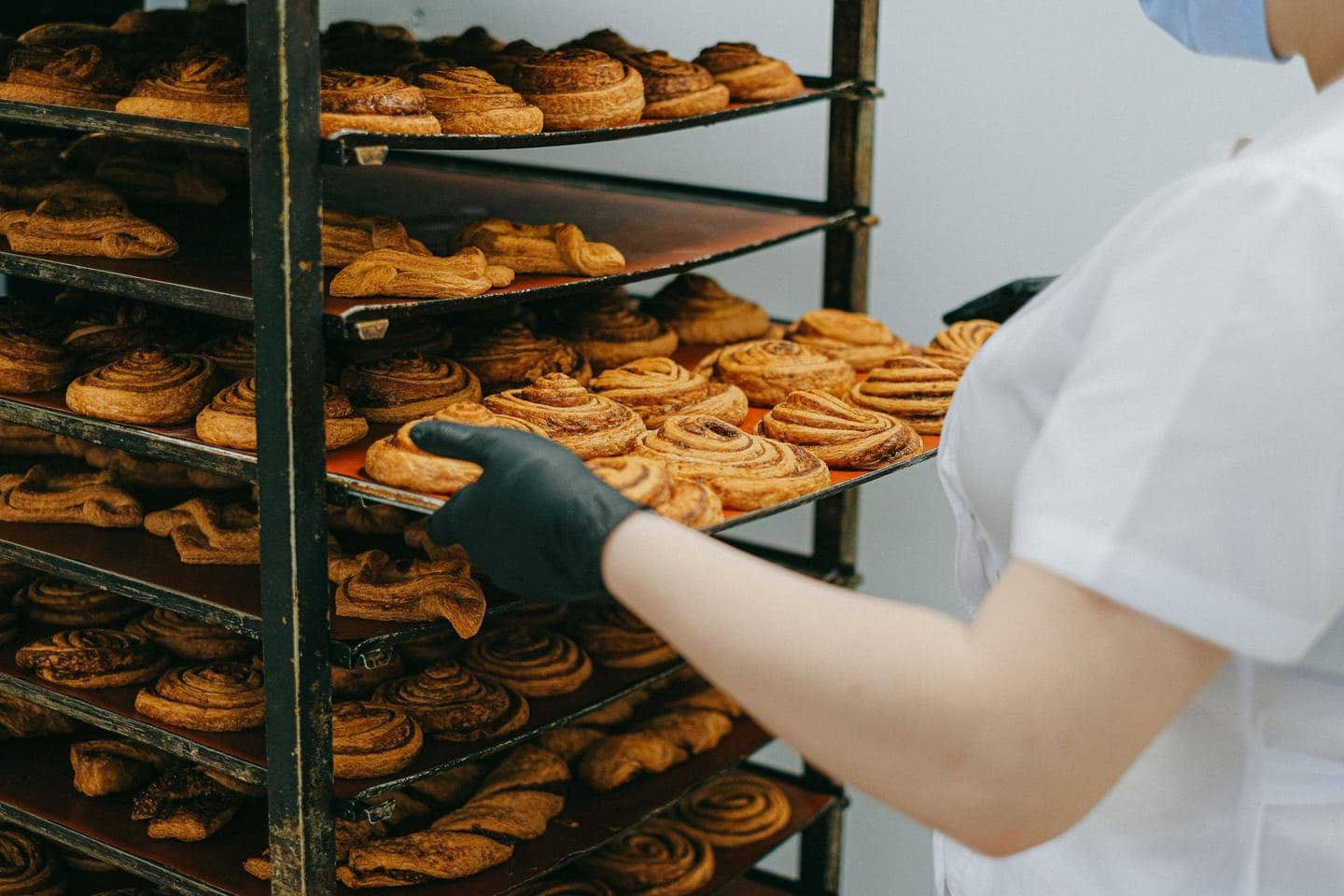A baker lifting a tray of fresh cinnamon buns onto a cooling rack