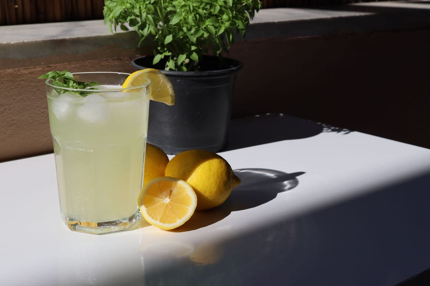 A glass of lemonade with mint and cut lemons on a sunny table