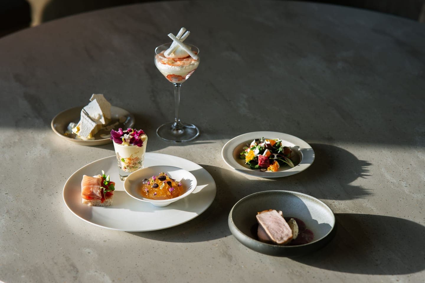Several small plates of food on a pale table, lit by soft natural daylight