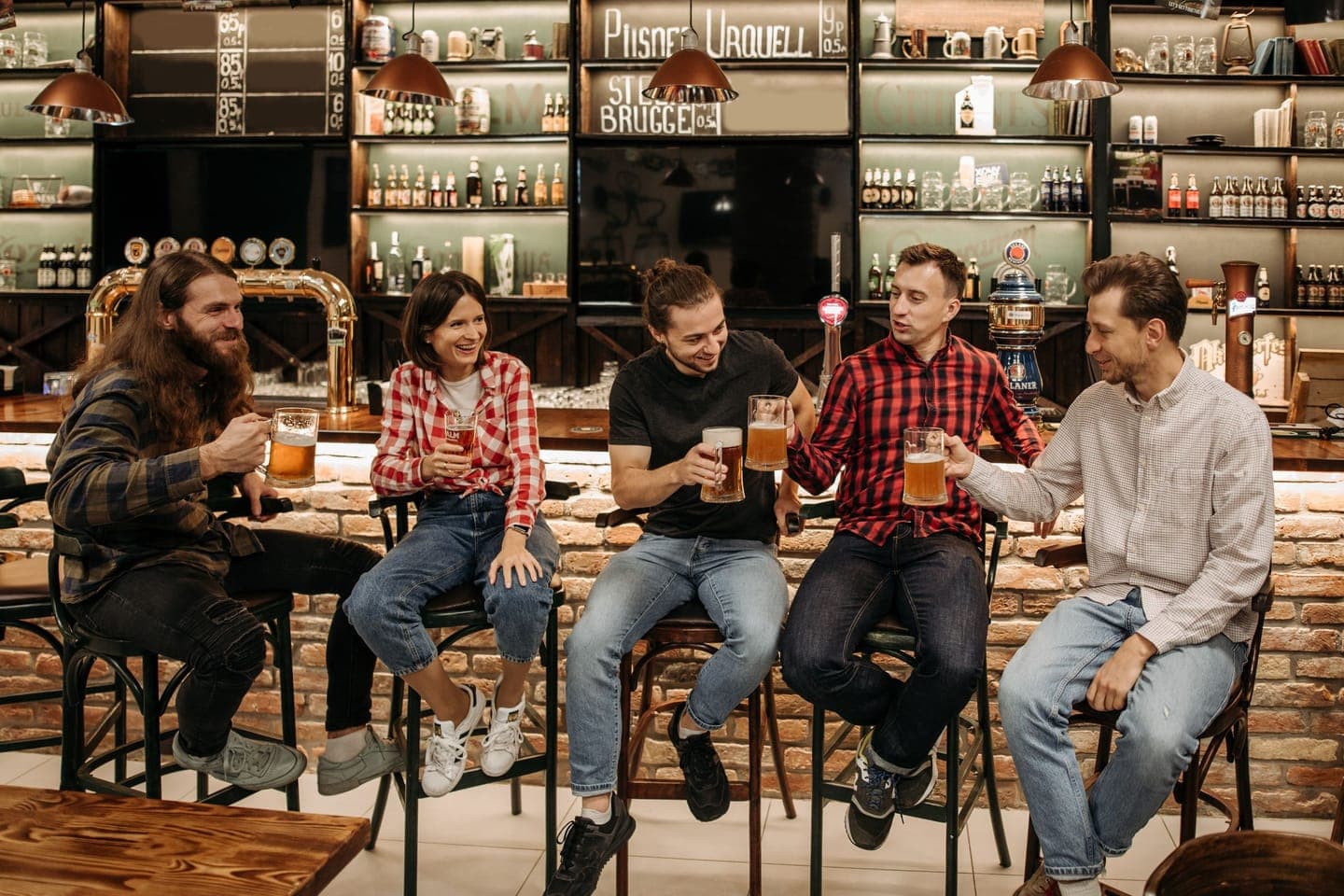 A group of friends with drinks sitting at a bar in front of the beer taps