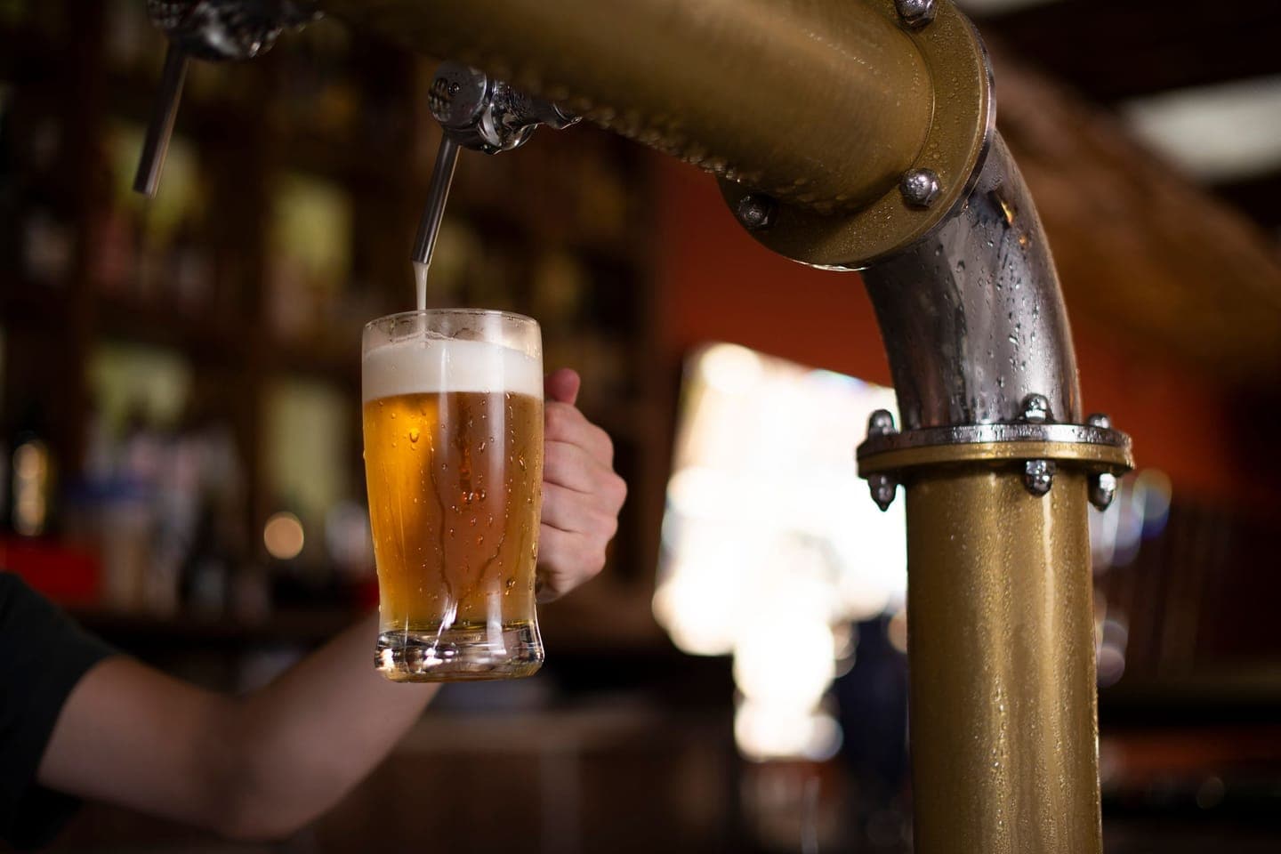 A pint of lager being poured from a brass tap behind a pub bar