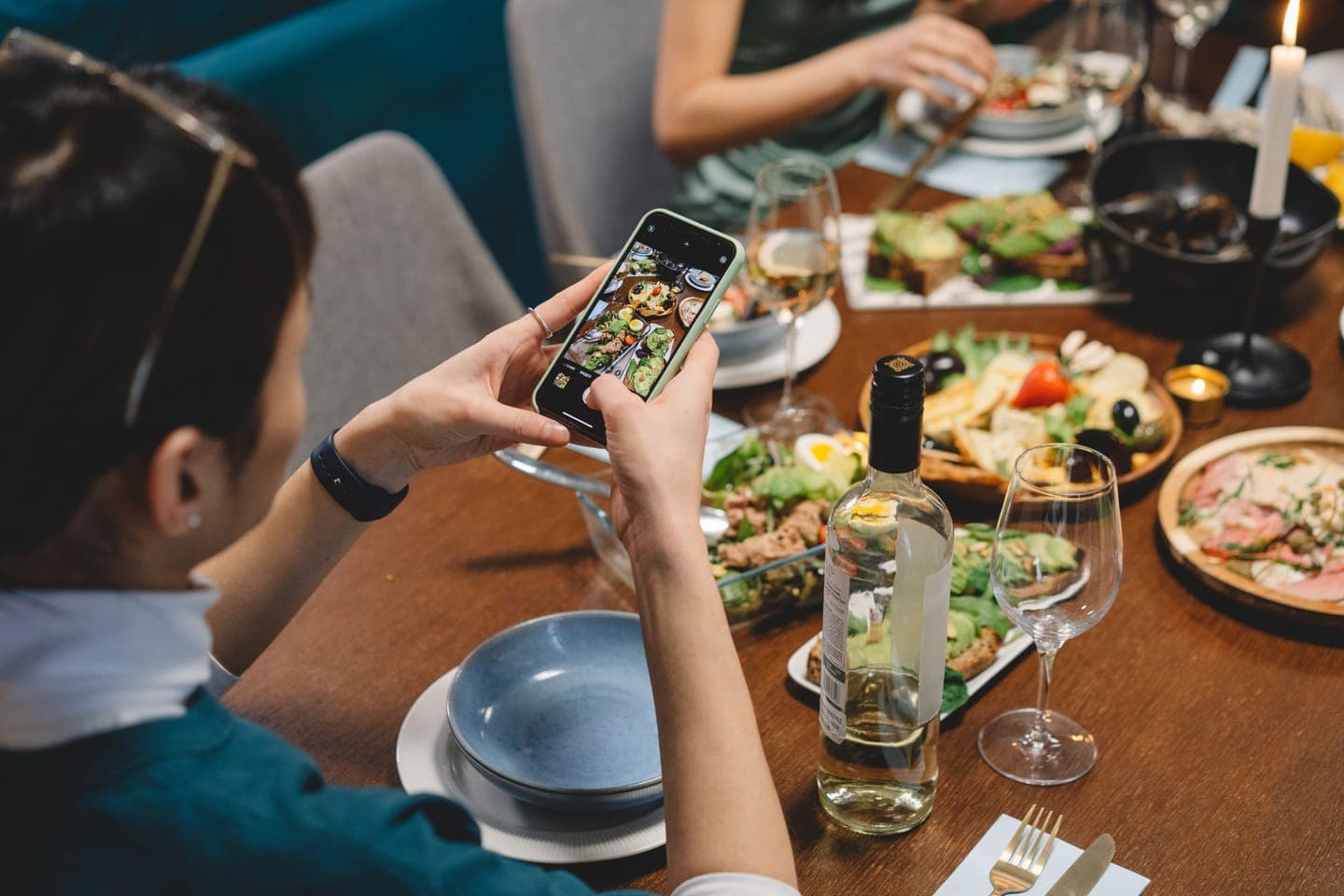 A diner photographing a table of dishes and wine with a smartphone