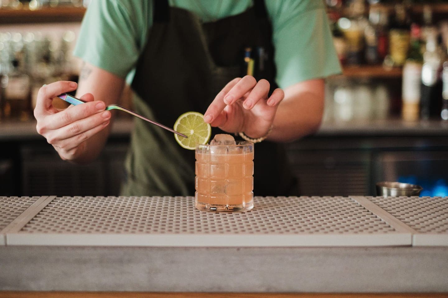 A bartender adding a lime garnish to a cocktail on the bar